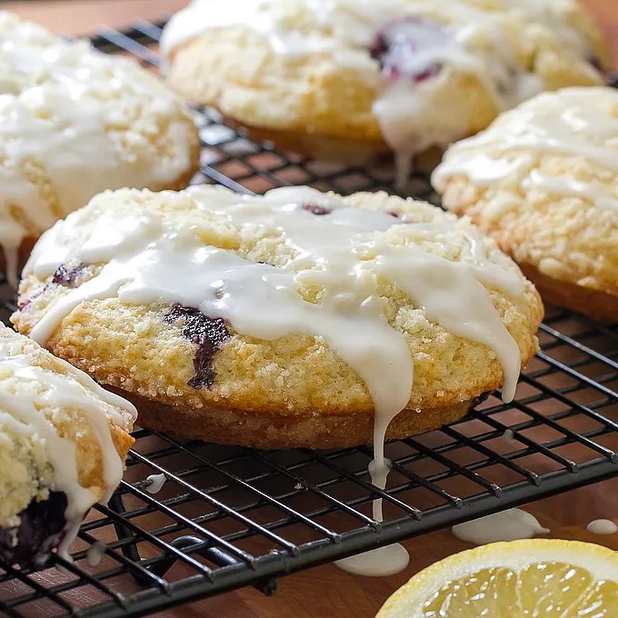 Close-up of freshly baked scones drizzled with icing on a wire rack, with a lemon slice in the foreground.