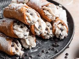 A plate of freshly made cannoli filled with sweet ricotta cream and chocolate chips, dusted with powdered sugar.
